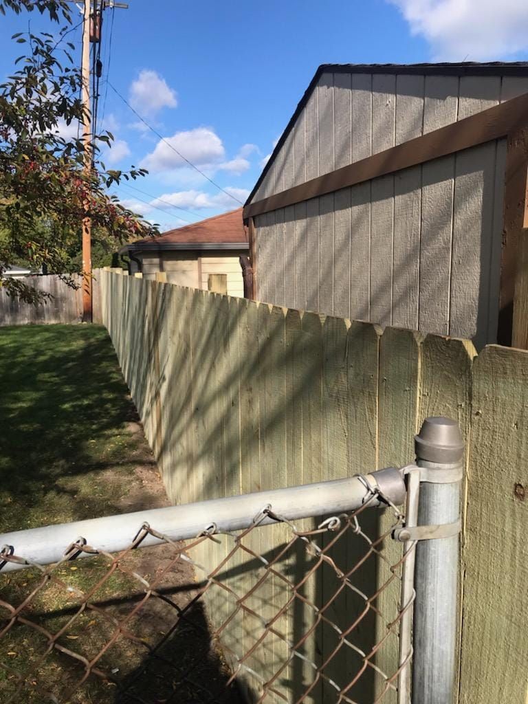 A wooden fence with a chain link fence in front of a house.
