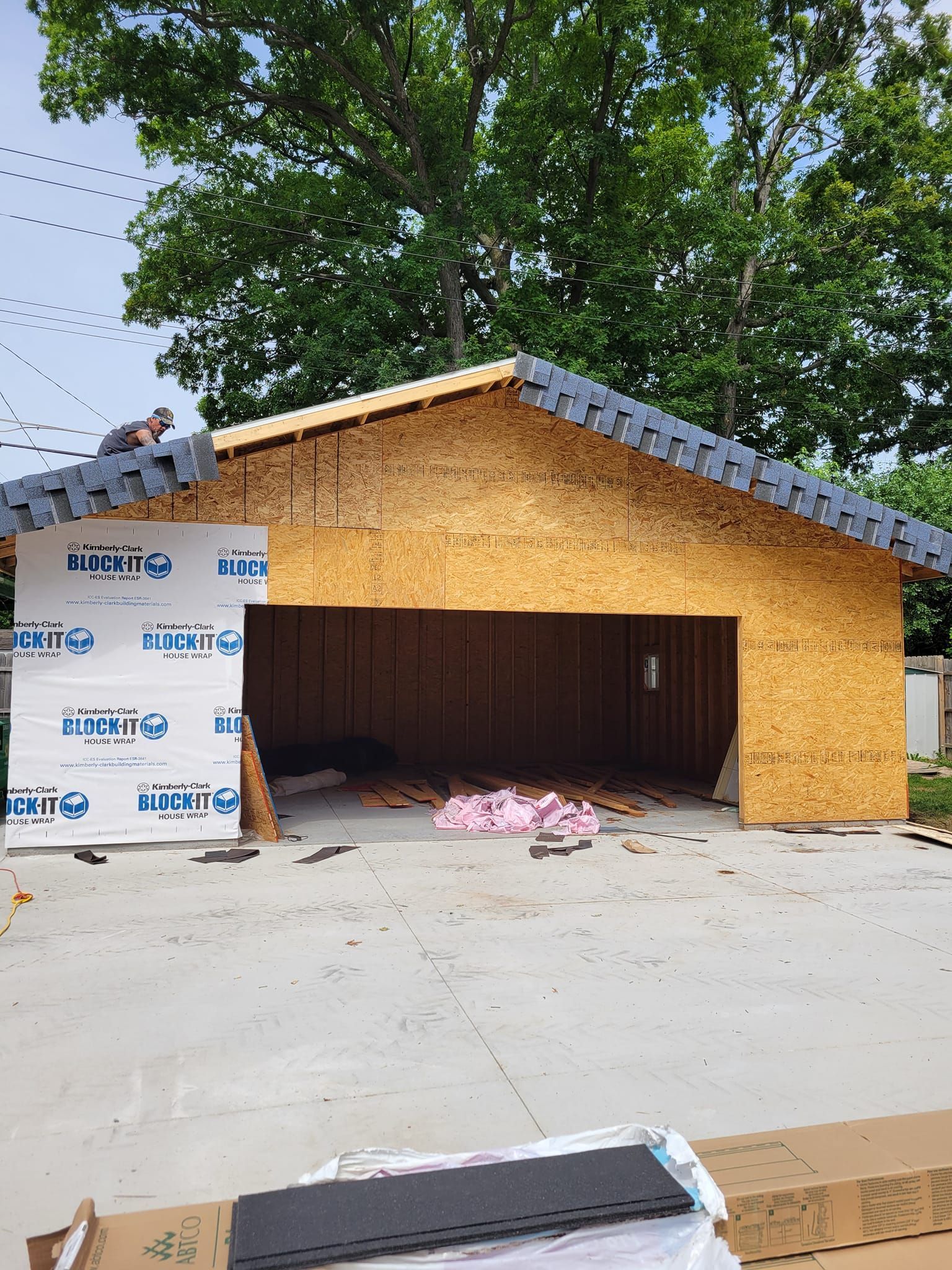 A man is sitting on the roof of a garage under construction.