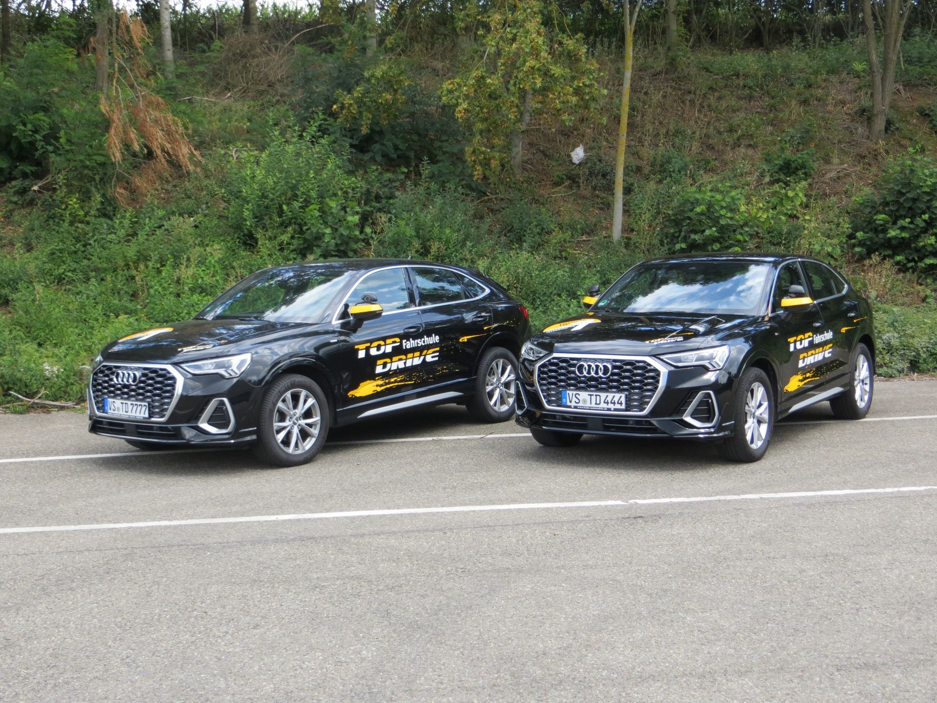 Zwei schwarze Autos stehen nebeneinander am Straßenrand.