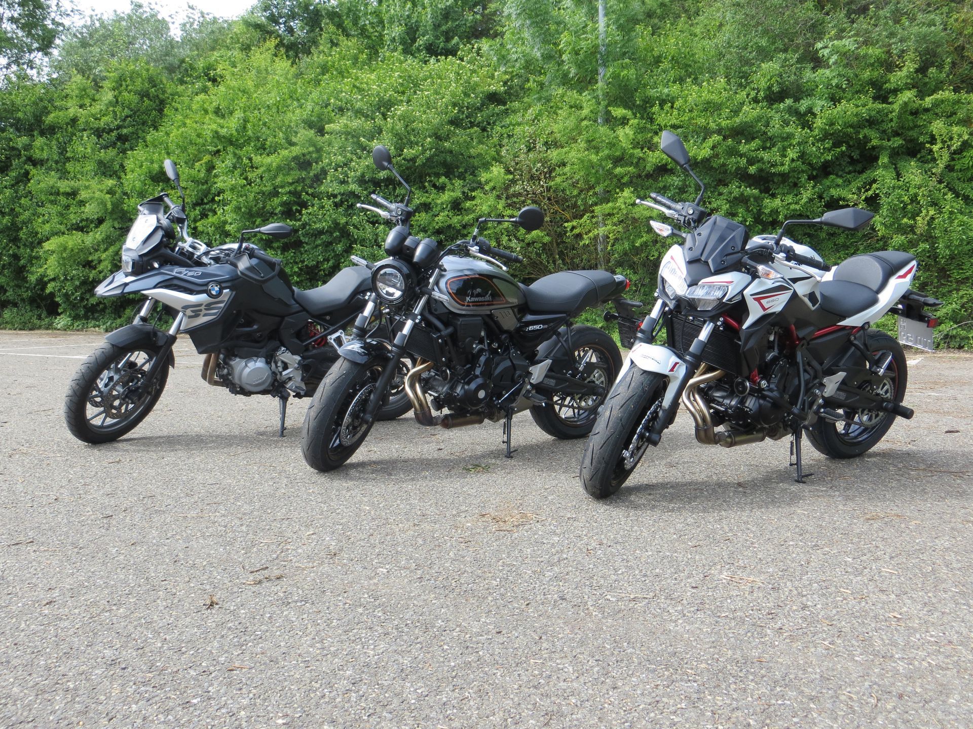 Auf einem Parkplatz stehen drei Motorräder nebeneinander.