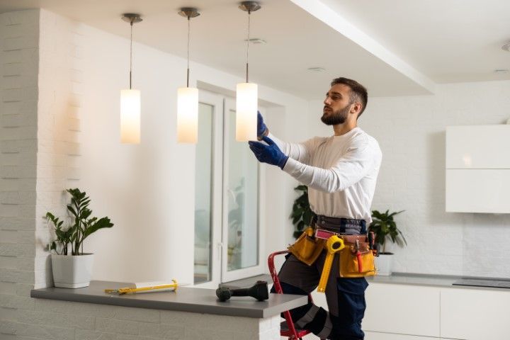 Electrician on a ladder installing a light fixture in a modern kitchen.