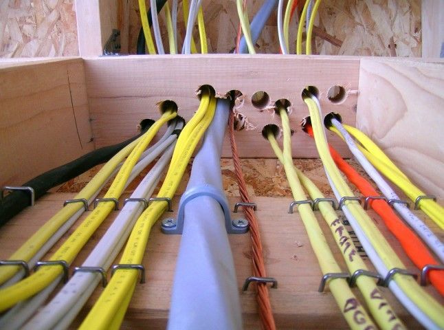 Electrical wires running through wooden framing, secured with metal clips.