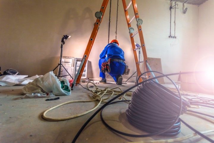 Electrician wiring cables, crouched on a construction site, near a ladder, orange and blue hues.
