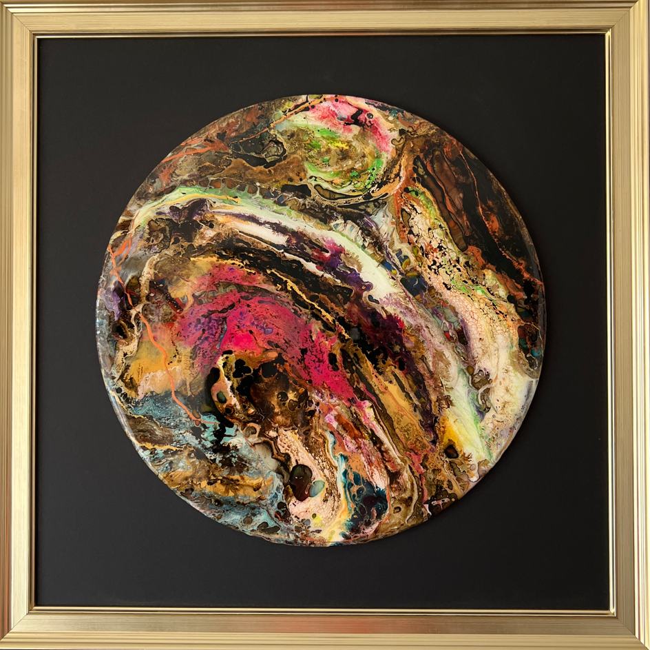 Cuadro abstracto circular en dorado, rosa y marrón, enmarcado en dorado sobre fondo negro.