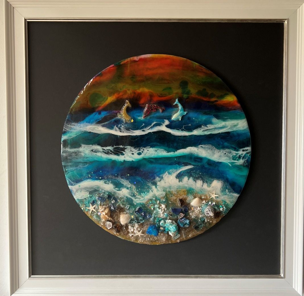 Escena oceánica en un marco redondo. Olas con delfines. Azul, verde azulado, naranja y blanco. Conchas marinas en el fondo.