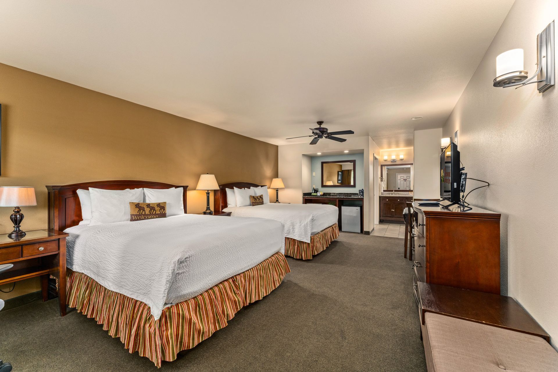 Hotel room with two beds, lamp-lit nightstands, desk, and TV in a carpeted suite