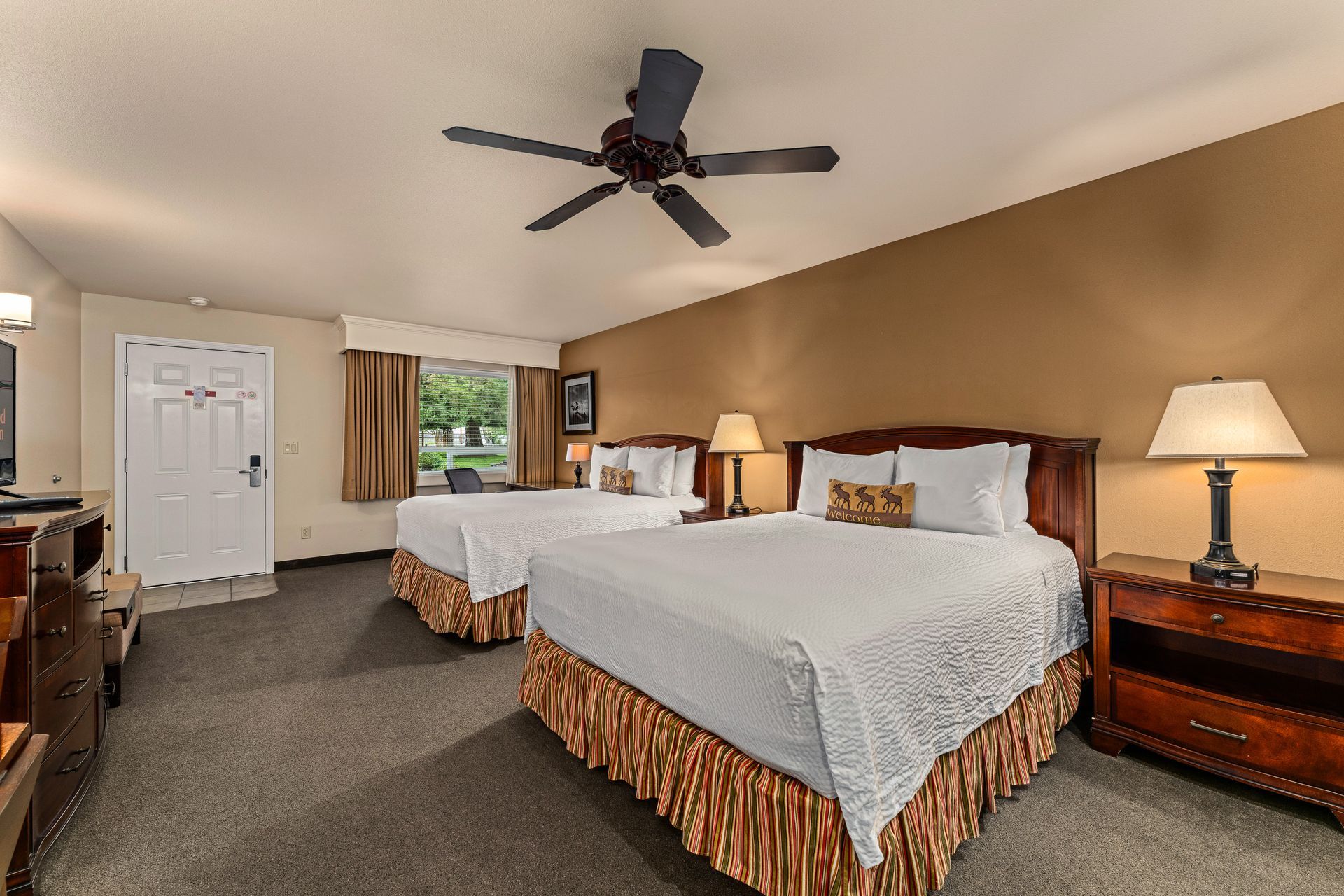 Hotel room with two queen beds, nightstands, ceiling fan, and window with curtains