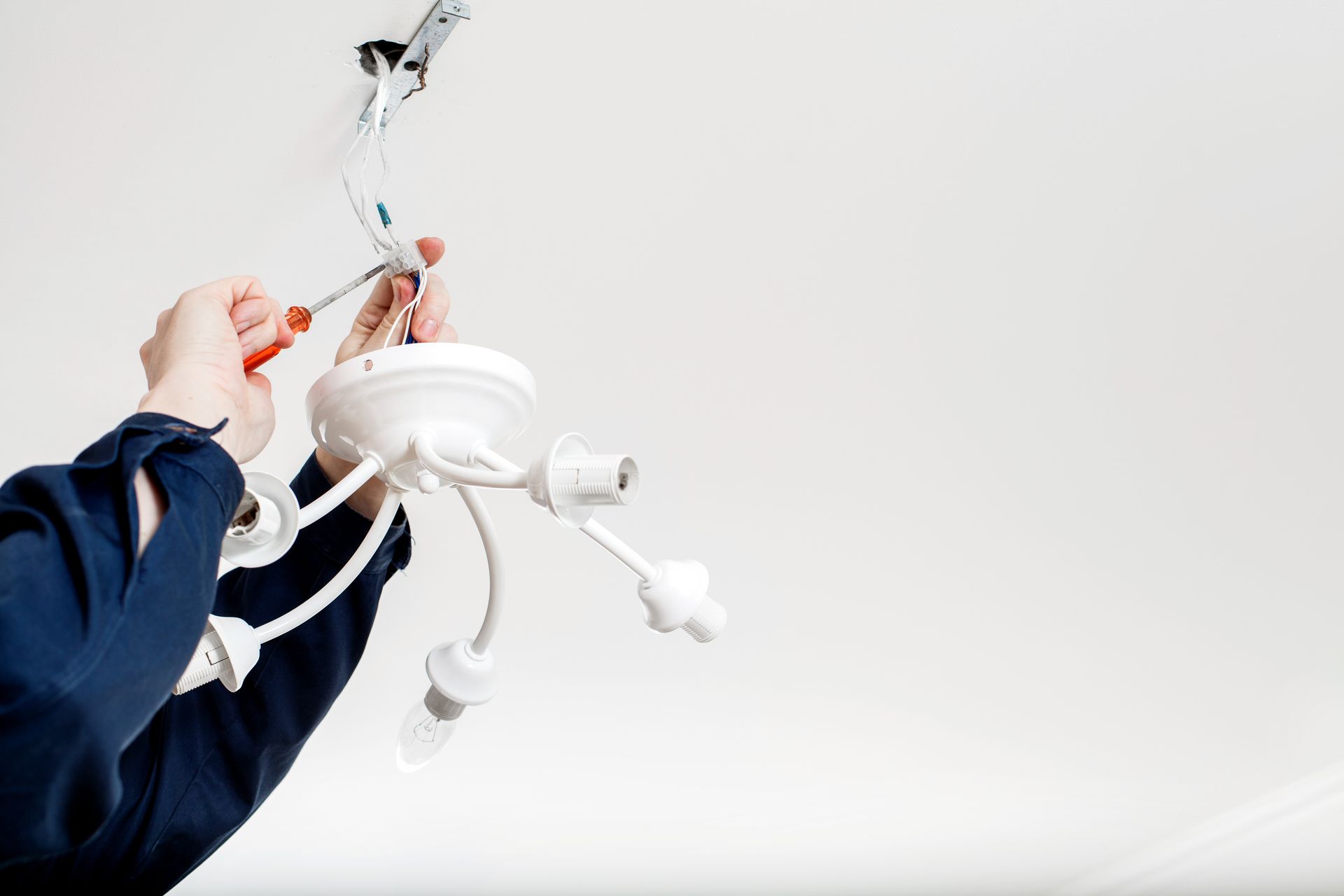 Person installing a white ceiling light fixture with exposed wires against a white ceiling