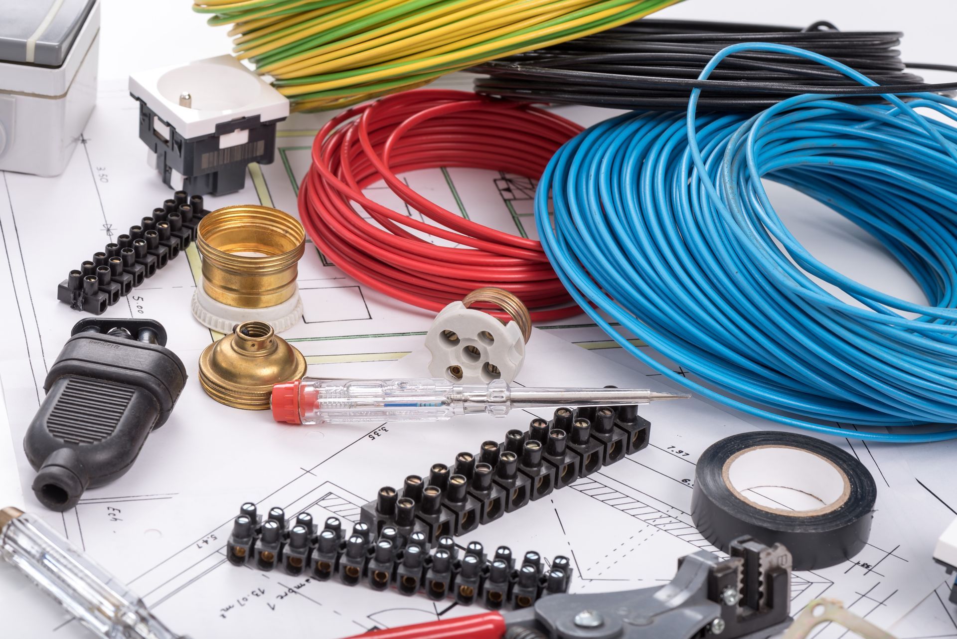 An array of electrical installation components, including colorful wiring, connectors, and tools atop architectural plans.