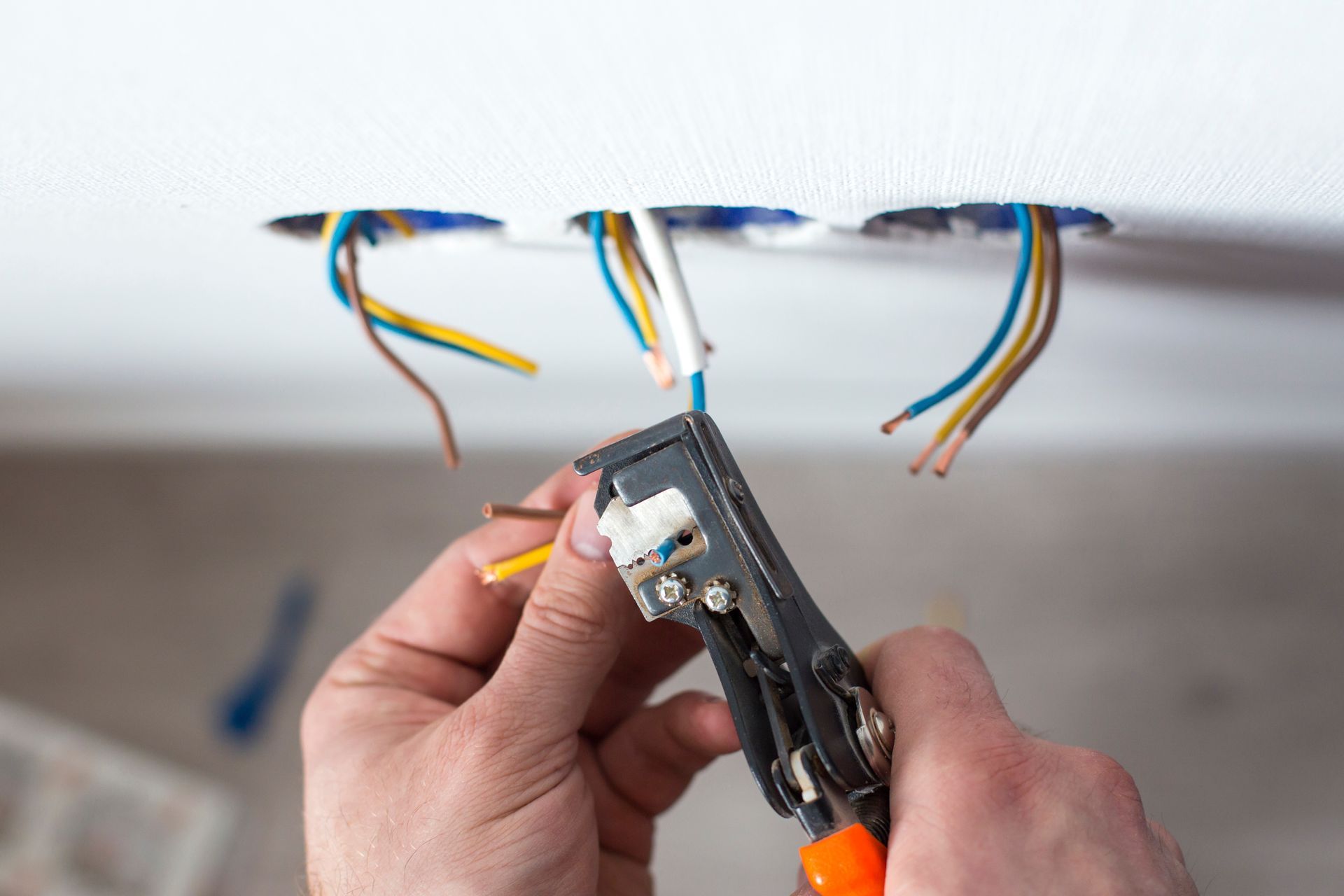 Hands stripping wires from a ceiling electrical box with a wire stripper tool