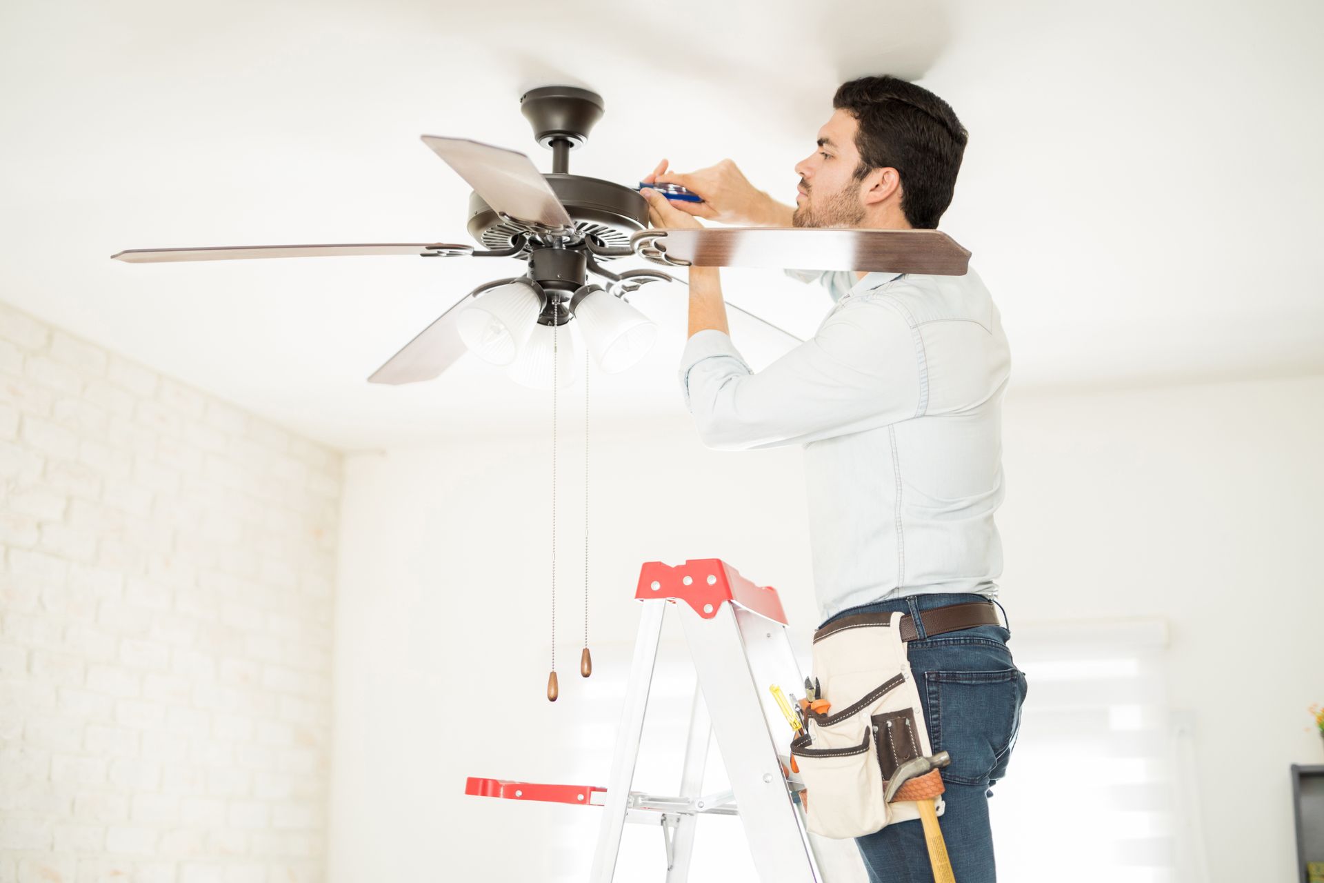 Man installing a ceiling fan on a ladder in a bright room