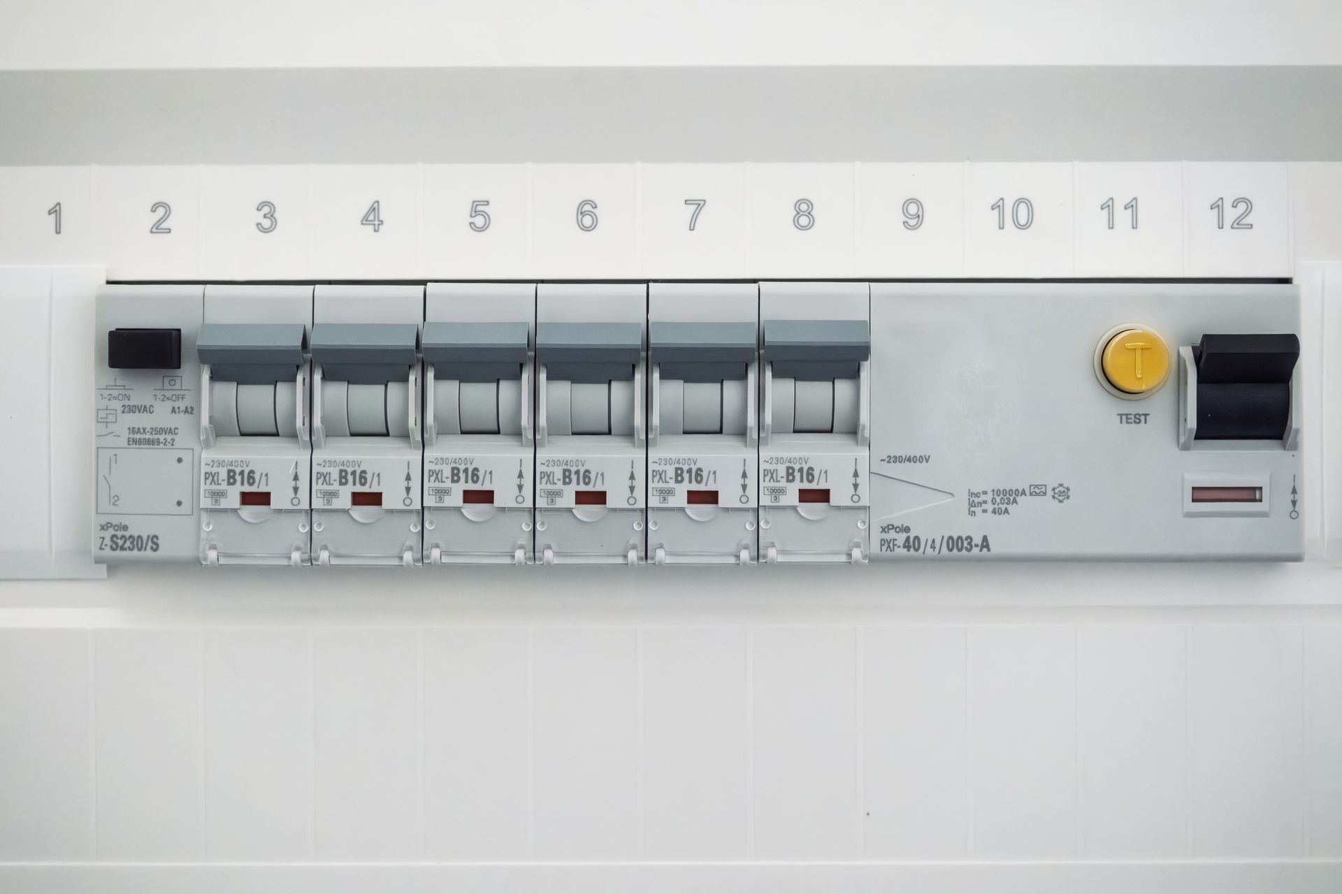 A white electrical distribution board featuring a series of circuit breakers, a test button, and numbered slots 1-12.