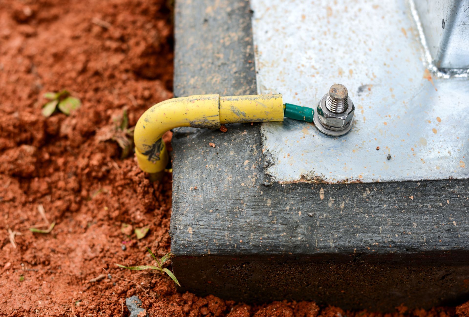 Yellow and green grounding wire attached to a metal base on red soil