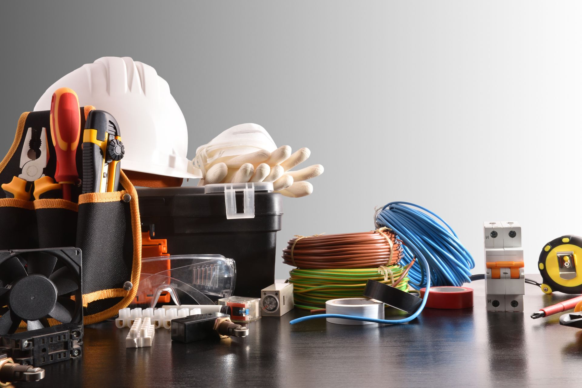 A white hard hat, tool belt with screwdrivers, spools of colored electrical wire, and various electrical components.