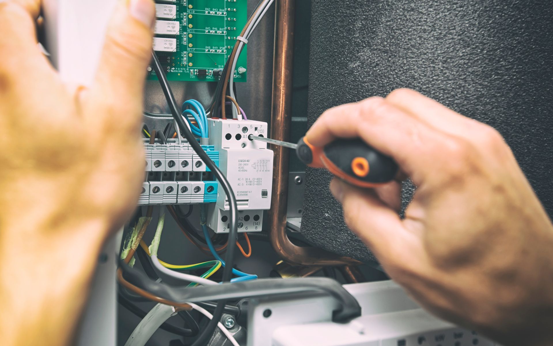 A person using a screwdriver to adjust wiring inside an electrical control panel for heating or air conditioning equipment.