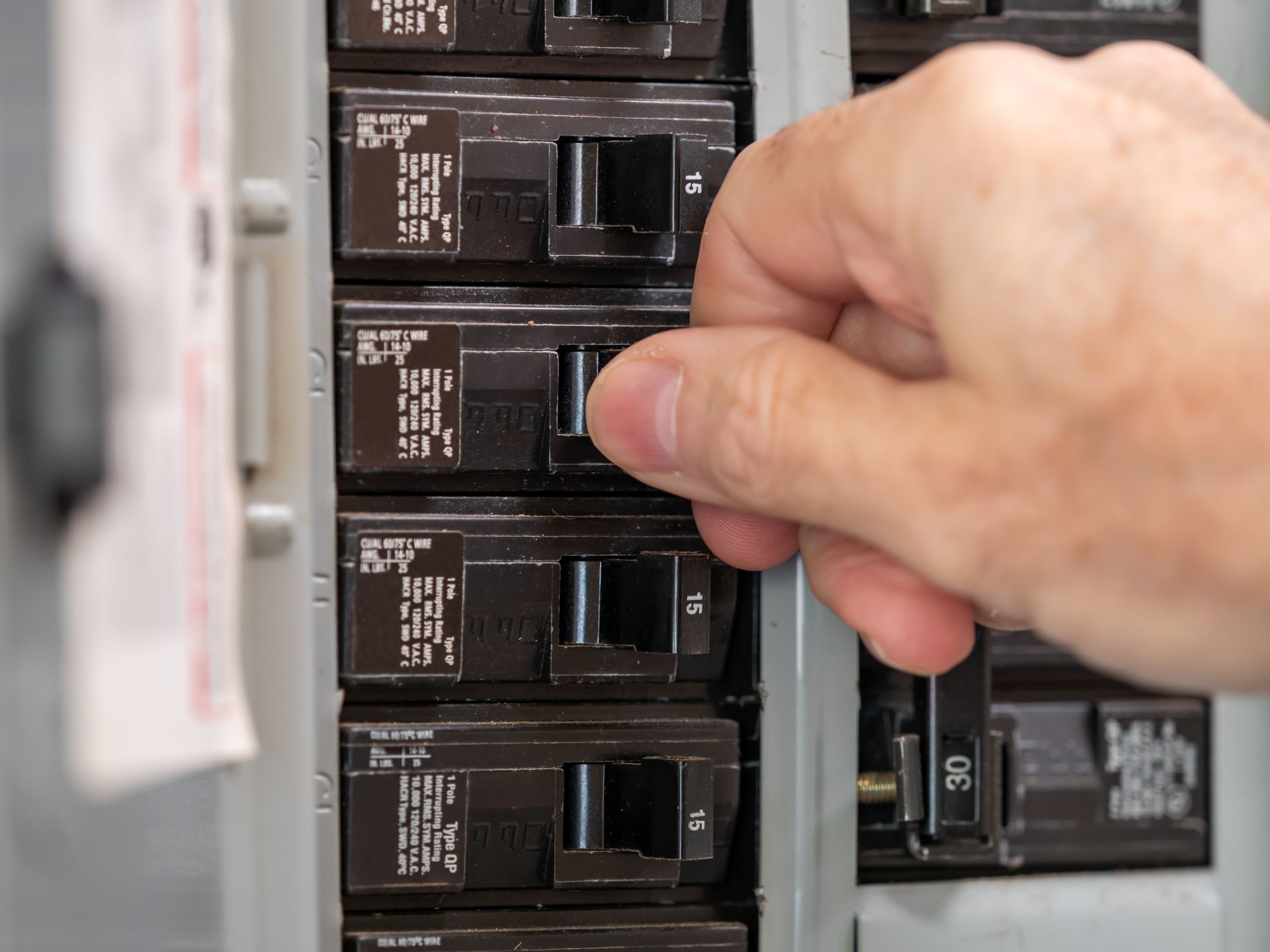 Hand turning on a switch in an electrical breaker panel