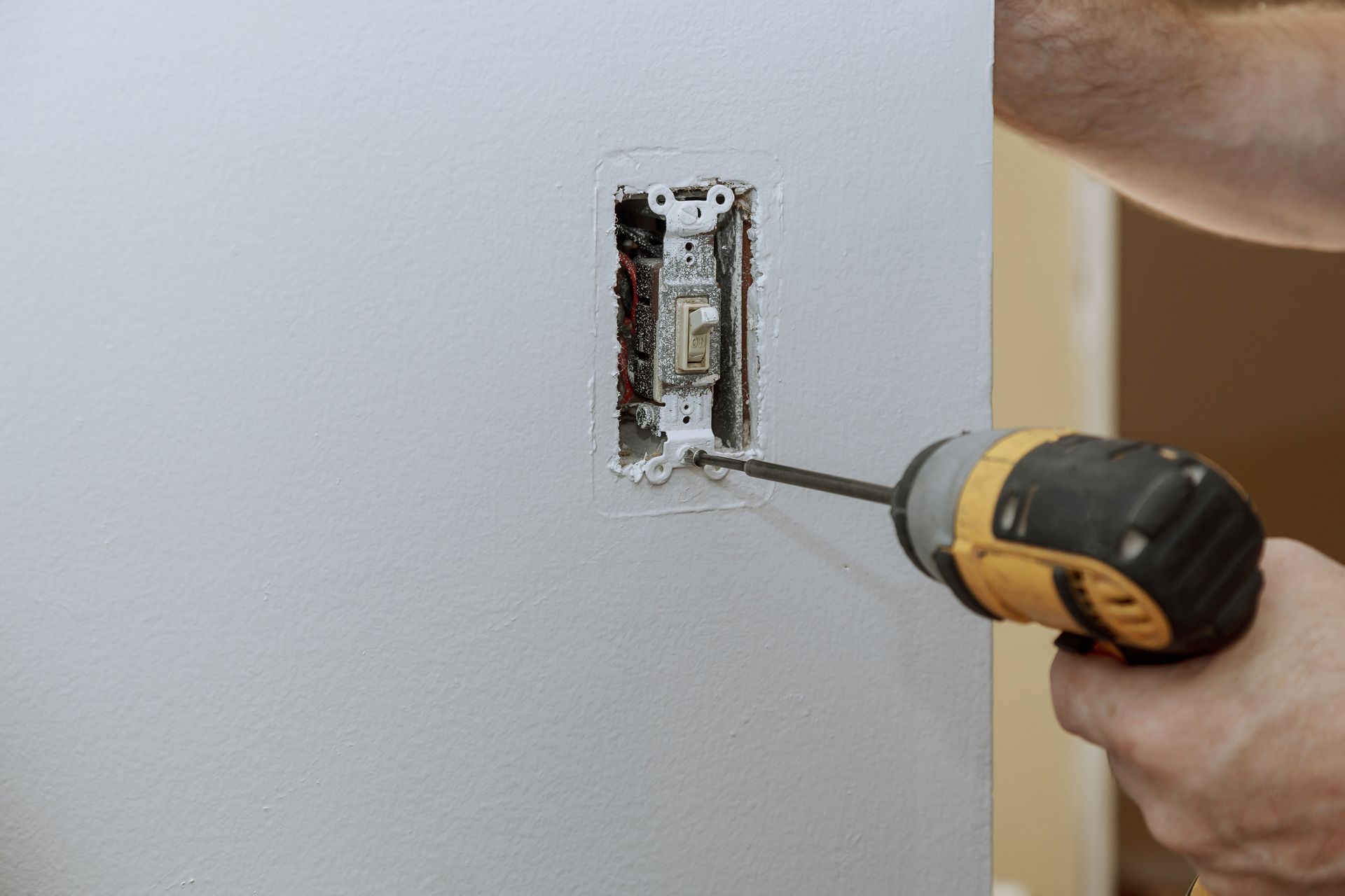 Hand using a screwdriver to remove an electrical wall outlet from a gray wall.