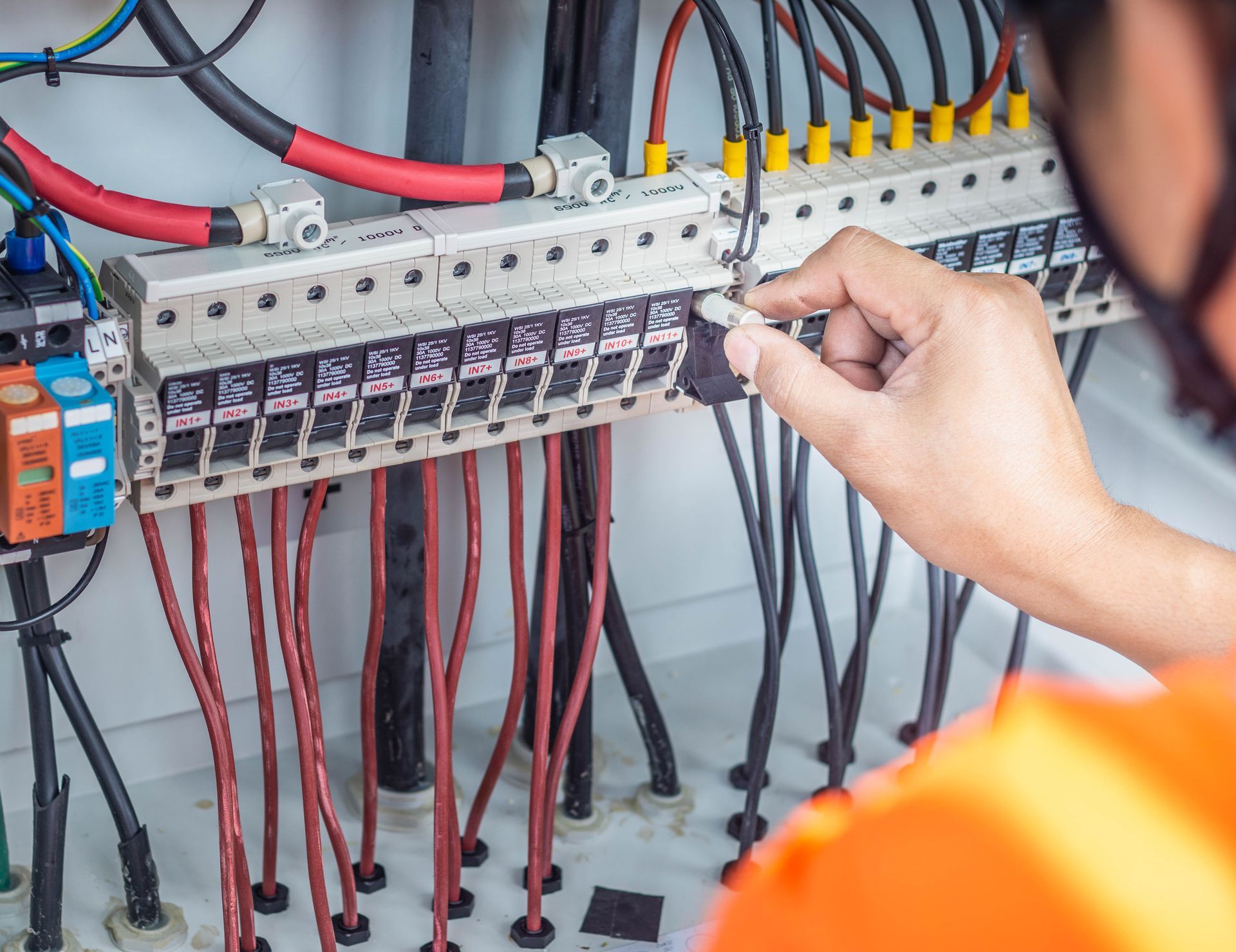 Electrician testing circuit breakers in a control panel with wires and switches.