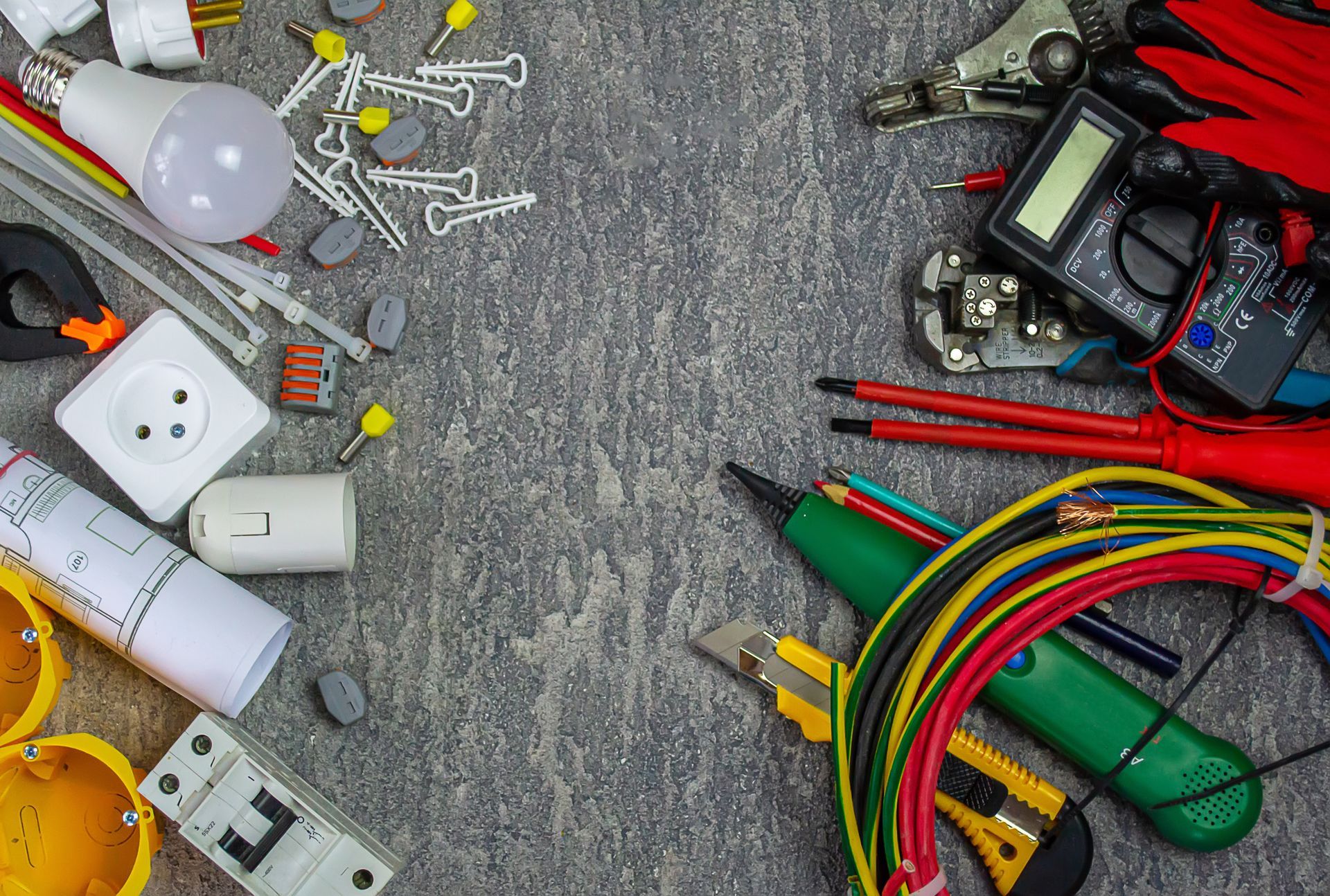 Assorted electrical tools, plugs, wires, and light bulbs arranged on a gray surface