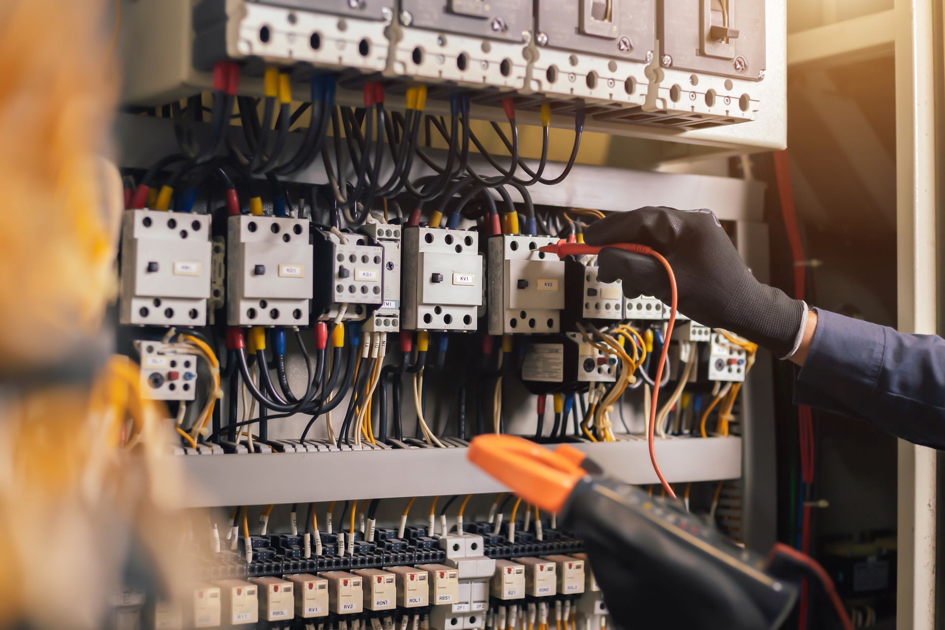 Electrician inspecting an open electrical control panel with wiring, breakers, and tools inside.