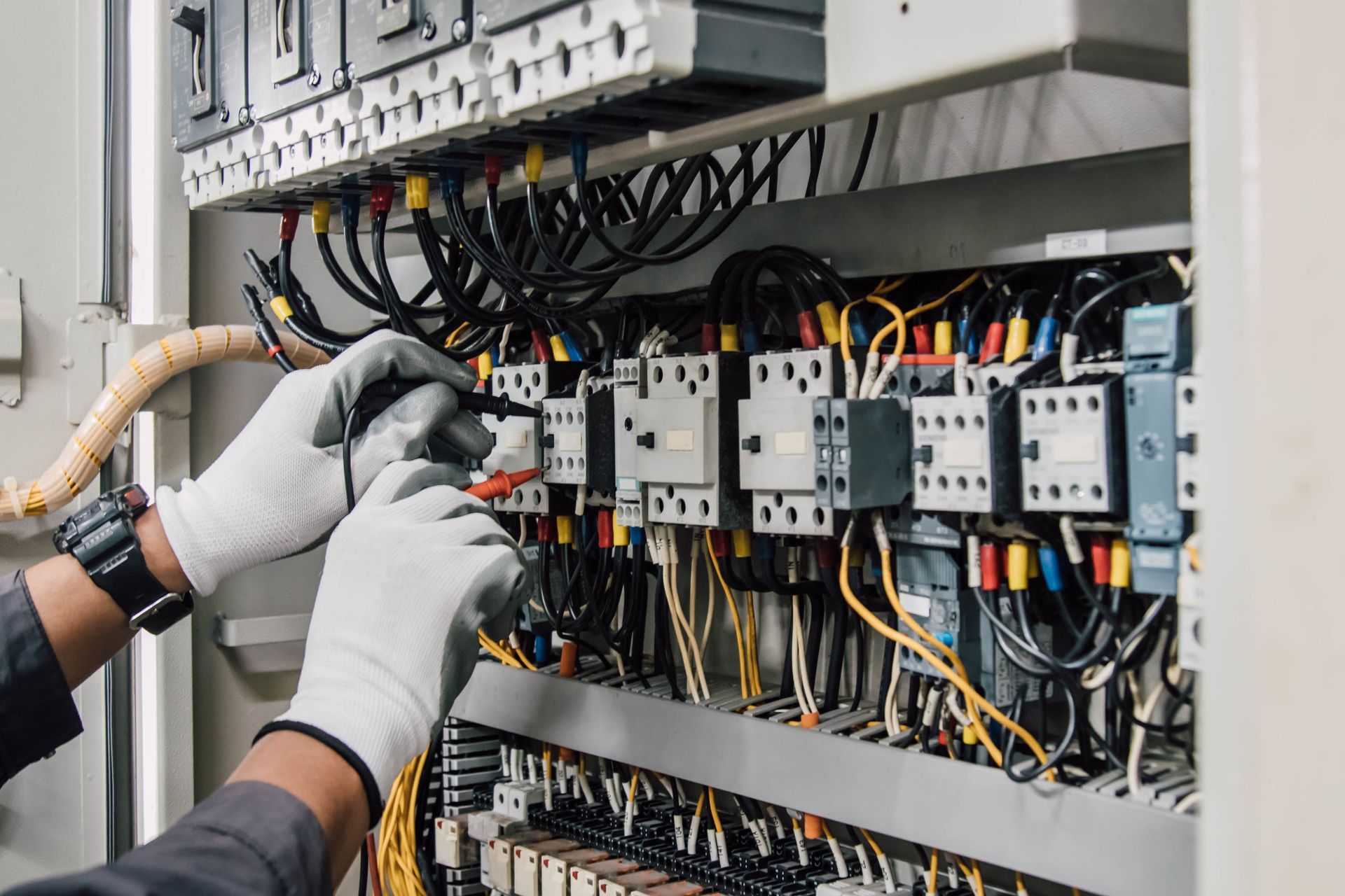 Technician testing wiring inside an electrical control panel with gloved hands