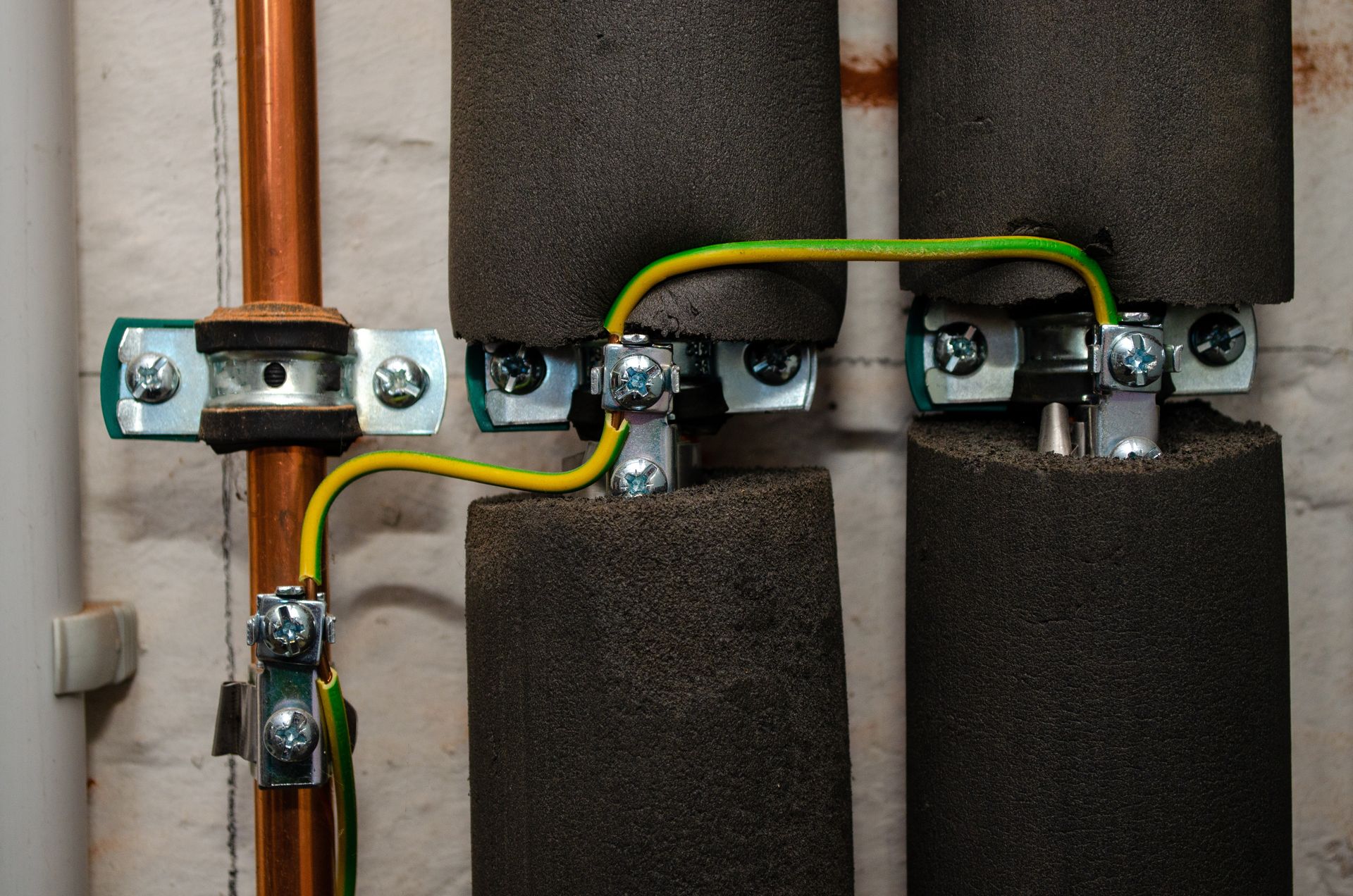 Copper pipes with black insulation foam are linked by green and yellow earth bonding wires attached with metal clamps.