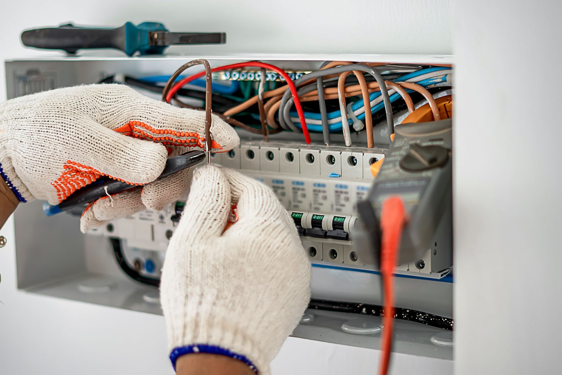 Gloved hands wiring an electrical panel with colorful cables and tools.