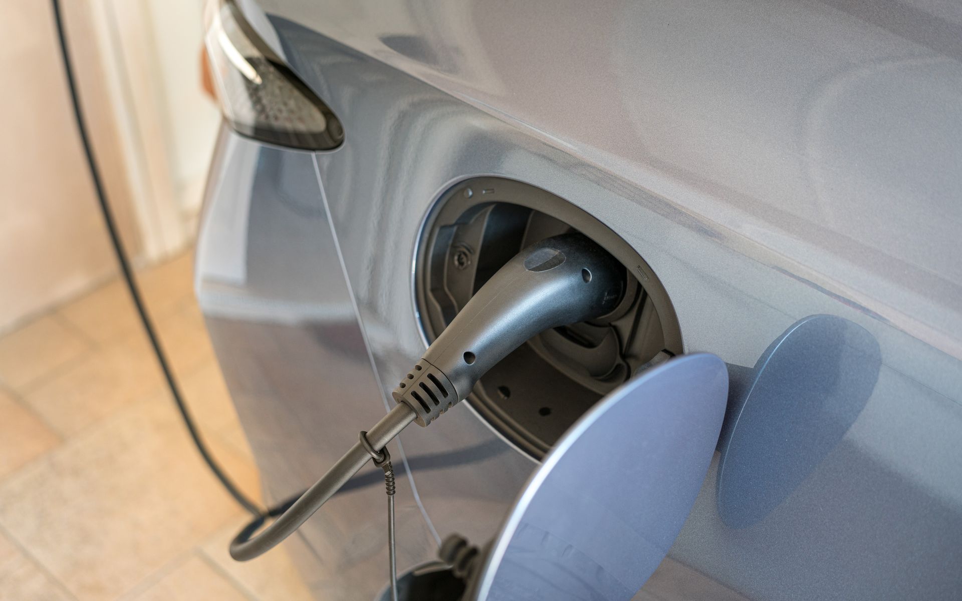A grey electric vehicle parked indoors with a charging cable plugged into its side charging port.