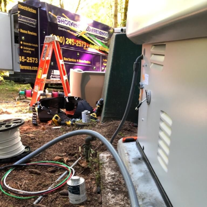 An electrician's work site with a generator, wiring, and a branded service van in a wooded outdoor area.