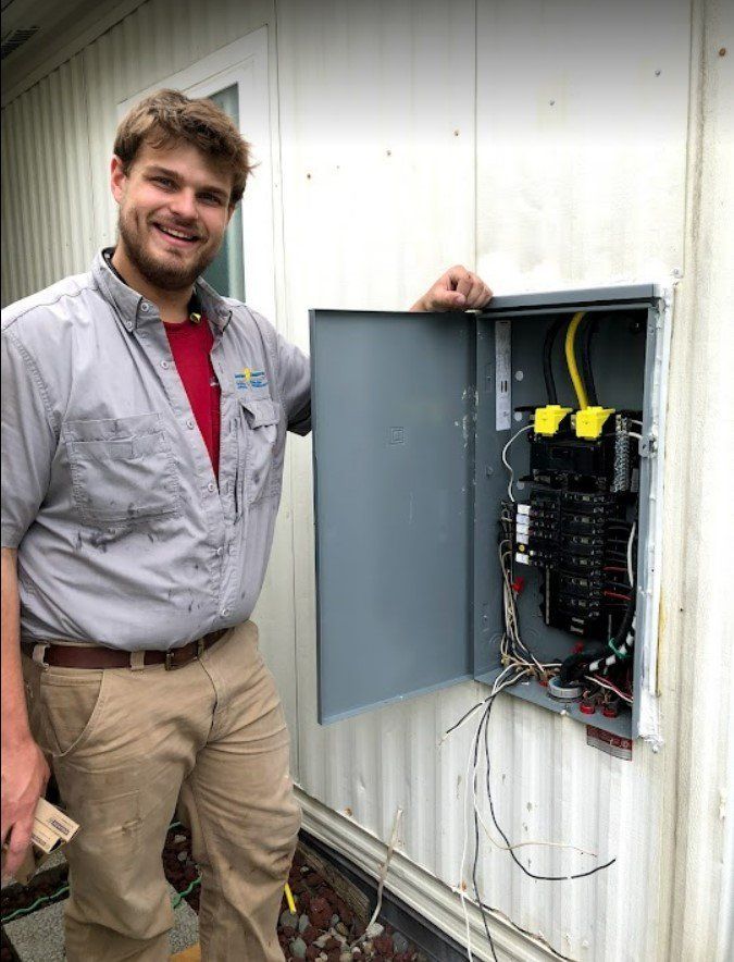 Technician beside an open outdoor electrical panel on a white building, with wires and breakers visible.