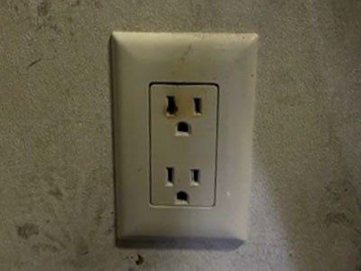 White electrical outlet on a beige wall, with one plug socket showing dark discoloration.