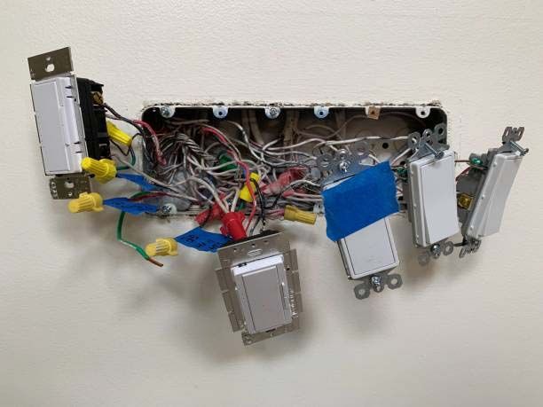Open wall electrical box with tangled wires and several outlets/switches mounted around it