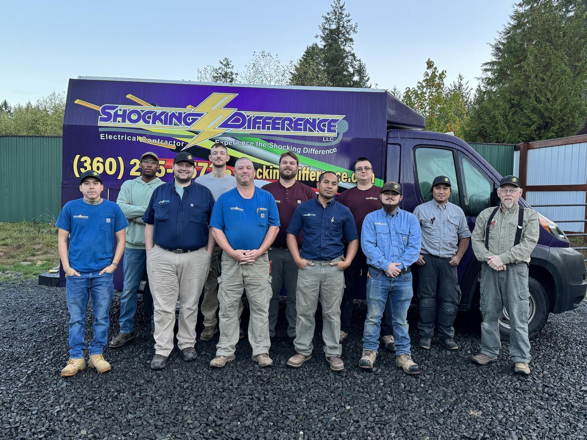 A group of eleven workers in matching uniforms stands in front of a purple branded 