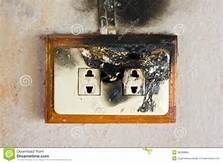 A damaged, charred double electrical wall outlet with black soot staining the surrounding wall.