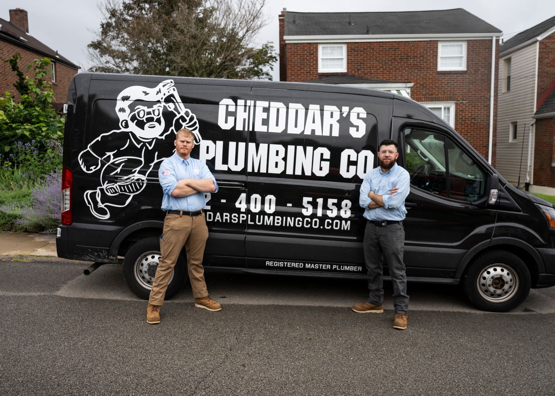 Two men standing in front of a black plumbing van. The van says 