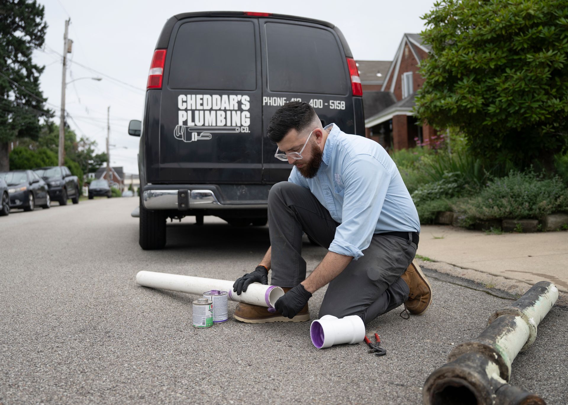 Plumber kneeling on street, working on pipes near his van.