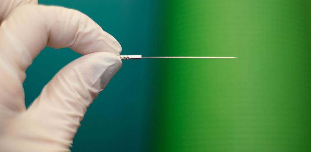 Gloved Hand Holding a Thin, Metal Medical Needle Against a Green Background — My Chiropractor Mackay City in Sarina, QLD