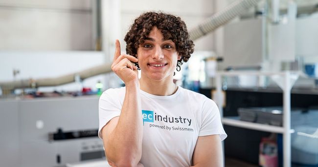 Ein junger Mann mit lockigem Haar trägt ein weisses T-Shirt mit der Aufschrift „Industrie“.