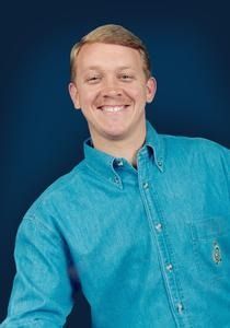 Man smiling, wearing a turquoise button-down shirt, blue background.