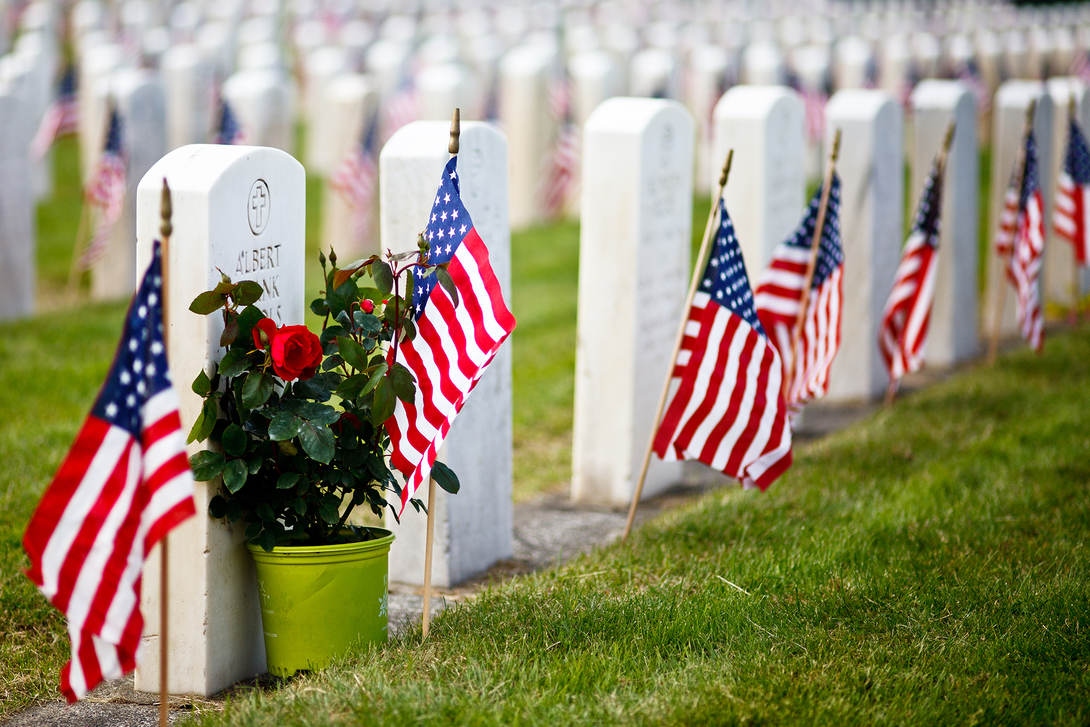 Rows of white headstones with American flags planted at each grave in a cemetery.