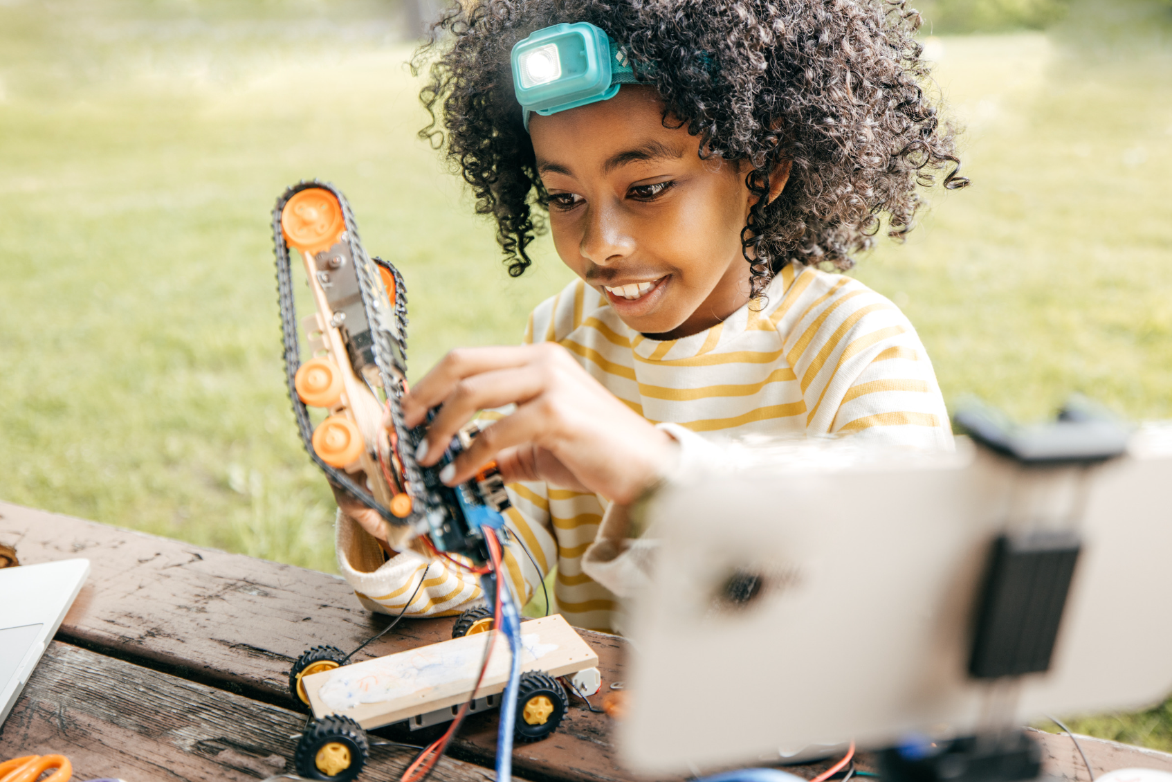 A young girl is sitting at a picnic table making a robot. Eden Creative Arts - Private Christian Micro School