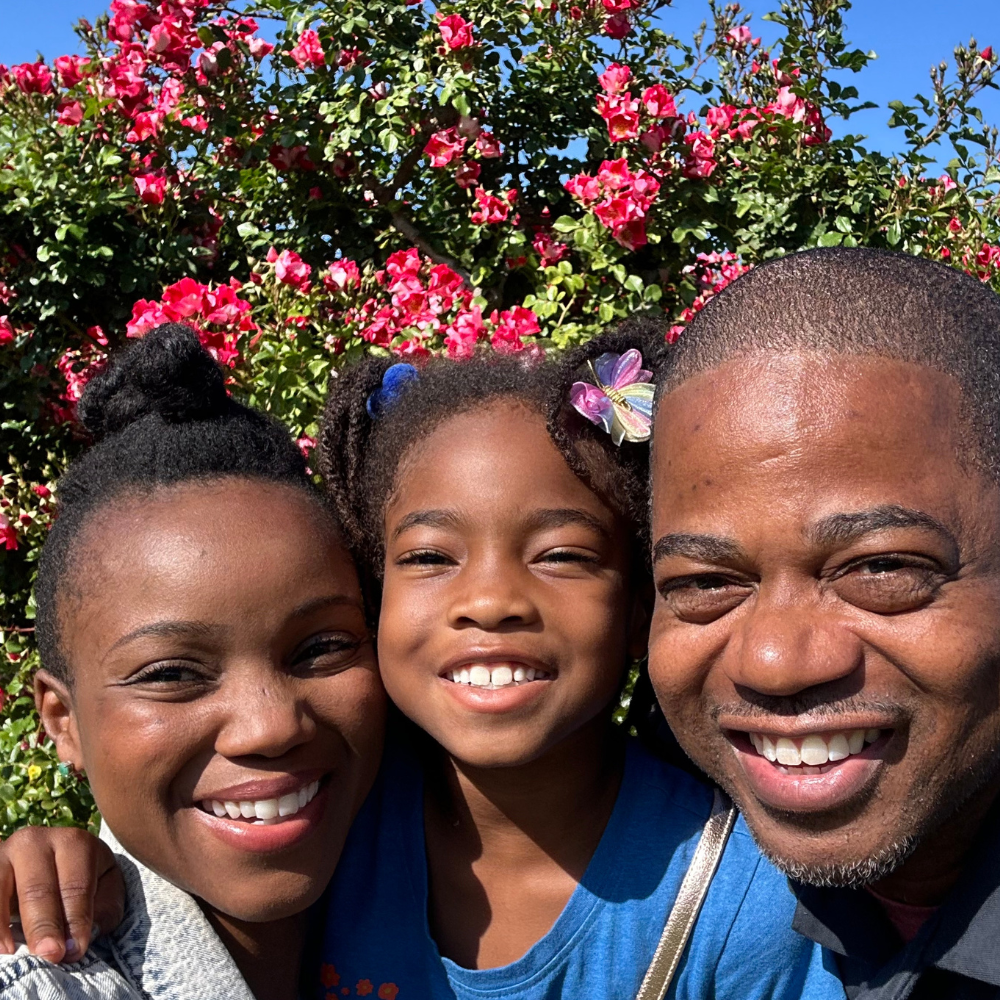 A family posing for a picture in front of a bush of red flowers