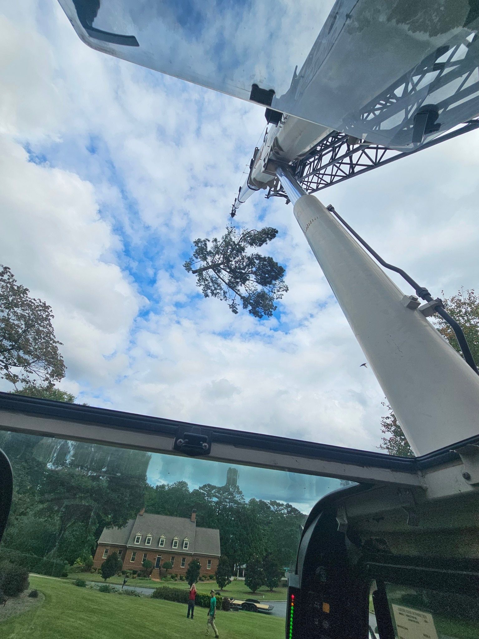 A crane lifting a tree limb in front of a house.