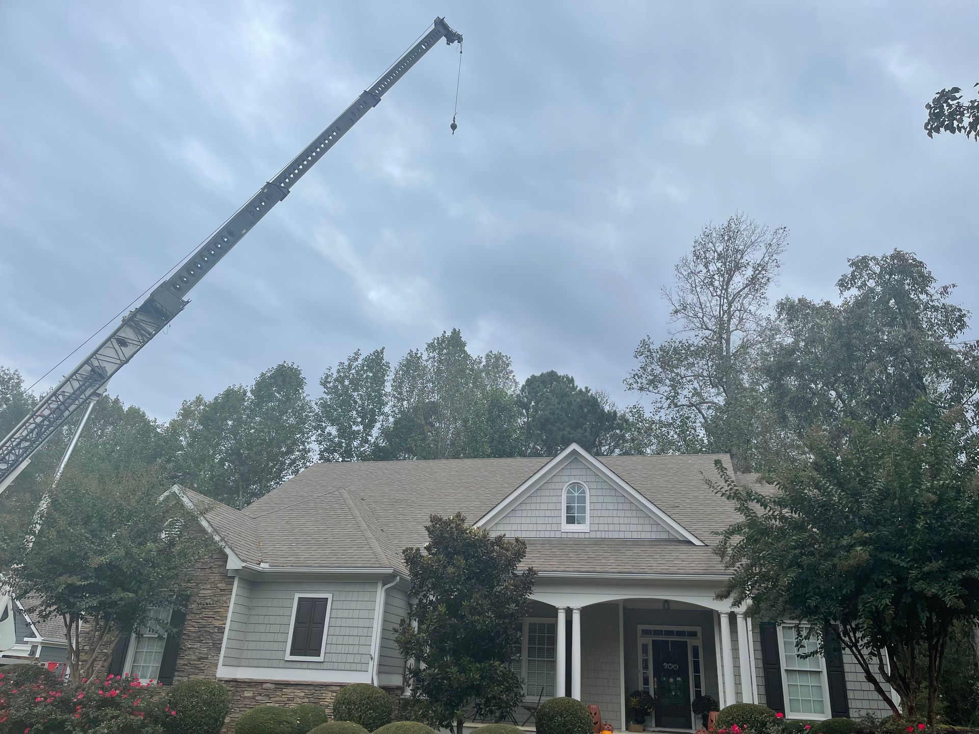 A crane is being used to remove a tree from the roof of a house.