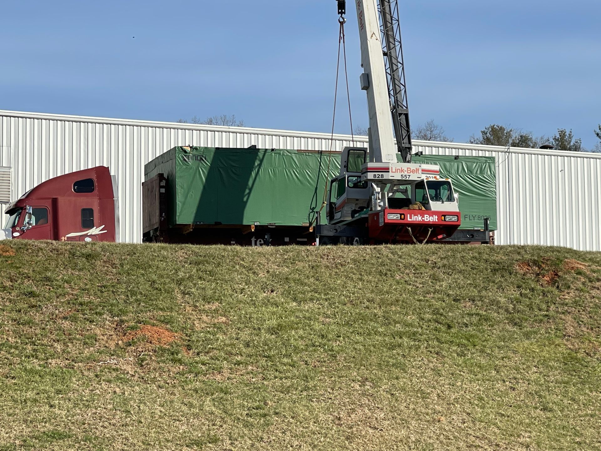A crane is lifting a green trailer in front of a building.