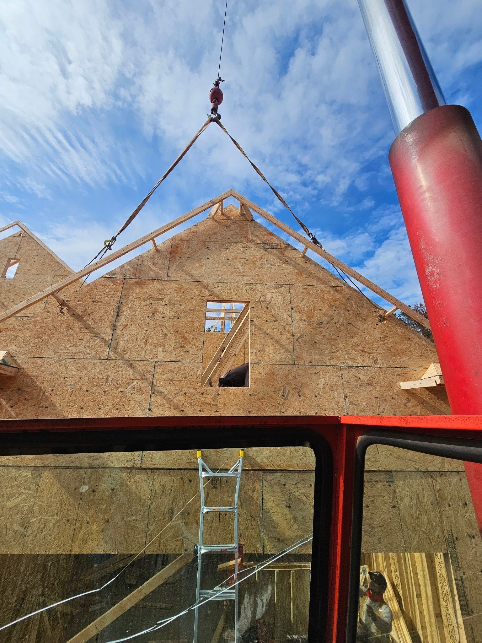 A crane is lifting a piece of wood on top of a building under construction.
