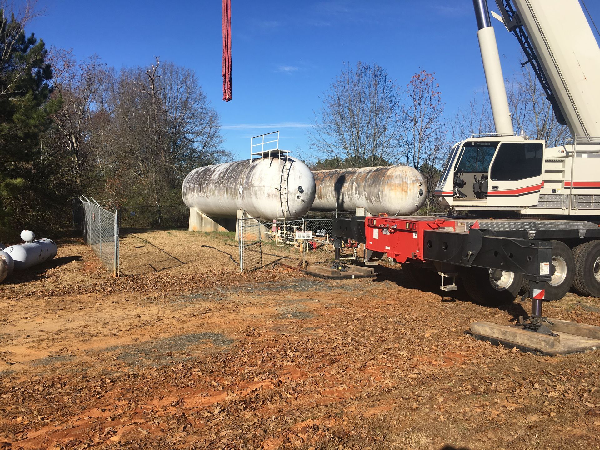 A large crane is lifting a large tank in a field.