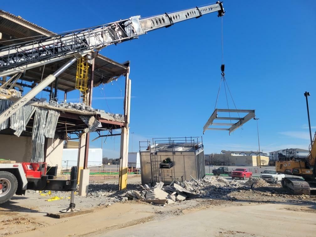 A crane is lifting a piece of metal in front of a building under construction.