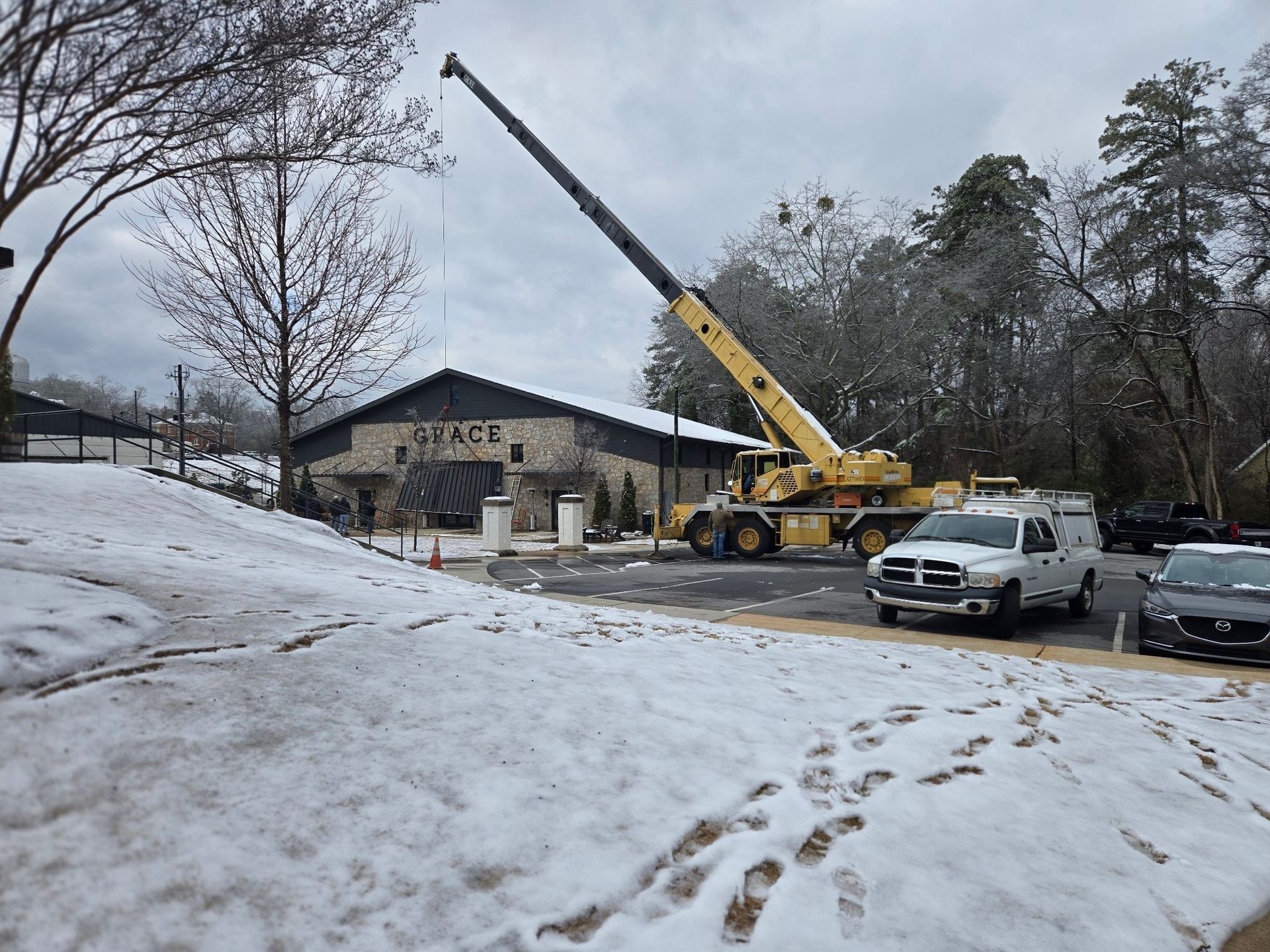 A truck is parked in front of a building with a crane in the snow.