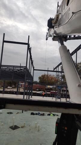 A crane is lifting a metal structure on top of a building under construction.